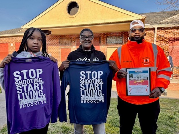 A man, woman and child stand together, holding t-shirts for Brooklyn Safe Streets